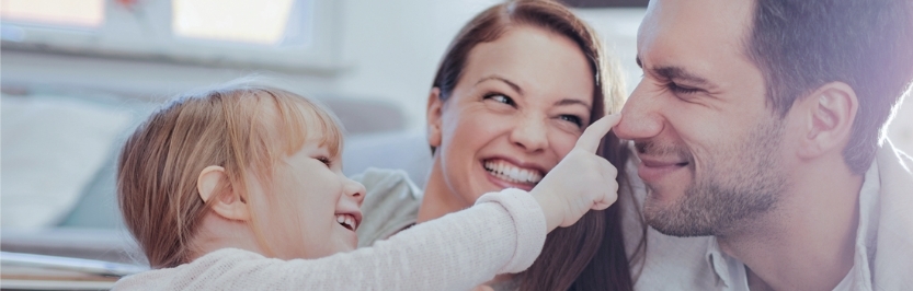 A child playfully touches a man's nose while a woman smiles beside them